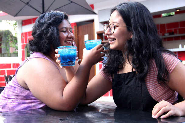 Due giovani donne latine brune di 20 anni bevono un cocktail blu gelido con chili, festeggiano bevendo alcol - Foto, immagini