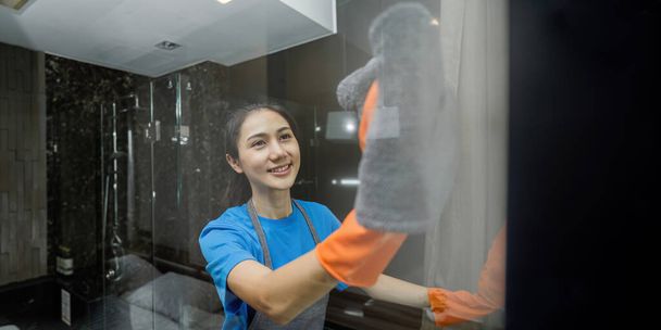 Καθαρισμός online υπηρεσία. Yong γυναίκα οικονόμος καθαρισμού καθρέφτη μπάνιο με ύφασμα. έννοια υπηρεσία καθαρισμού σπιτιού. - Φωτογραφία, εικόνα