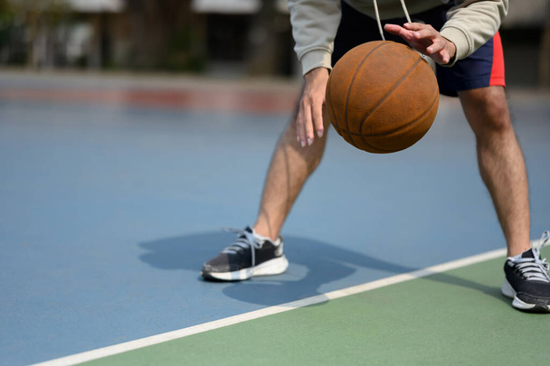 Gehakt schot van basketbalspeler stuiteren de bal op een buitenveld tijdens een zonnige dag. - Foto, afbeelding