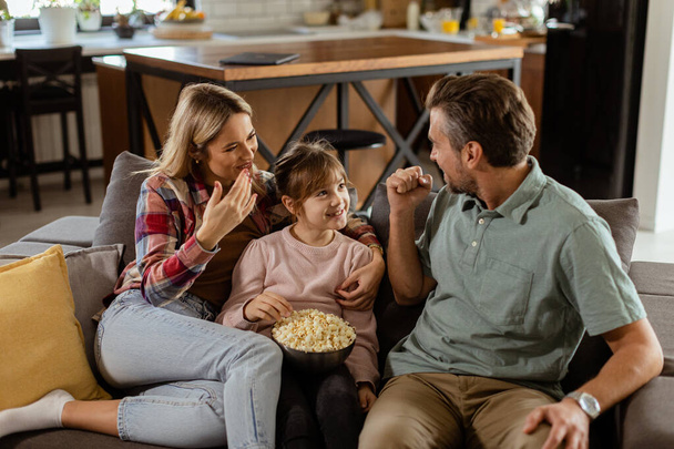 Una familia alegre descansa en el sofá, entablando una conversación lúdica con un tazón de palomitas de maíz - Foto, Imagen
