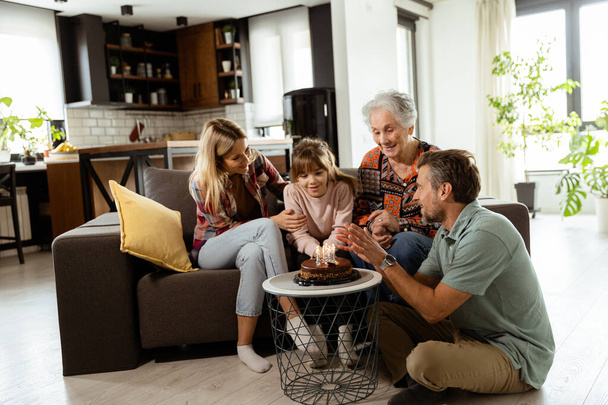 Szívmelengető jelenet bontakozik ki, ahogy egy többgenerációs család összegyűlik a kanapén, hogy egy szülinapi tortát mutassanak be egy boldog nagymamának, emlékeket teremtve, hogy ápolják - Fotó, kép