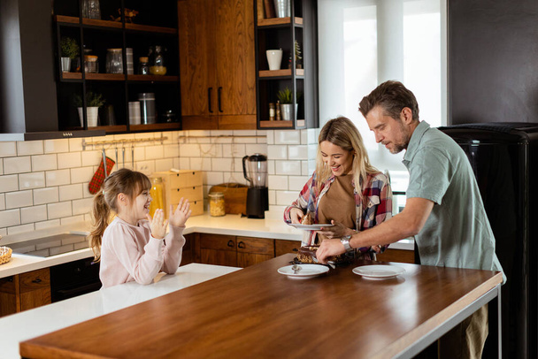 Egy szívmelengető jelenet bontakozik ki, ahogy egy család élvezi a szájba öntött csokitorta együtt a meleg napsütötte konyha, közös mosoly és emlékeket teremt - Fotó, kép