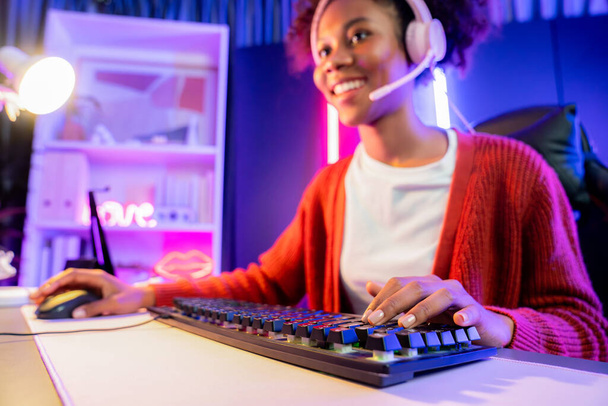 Afroamerykańska dziewczyna serpentyna gra online walki z Esport wykwalifikowany zespół noszenia słuchawek w neonowym kolorze oświetlenie pokoju. Rozmawianie z innymi graczami struganie strategii, aby wygrać konkurentów. Tastemaker. - Zdjęcie, obraz