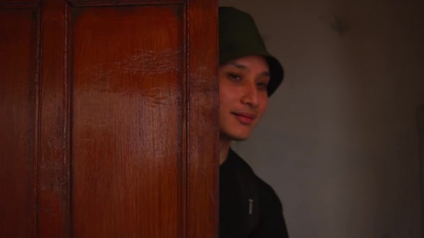 Retrato de um jovem em um chapéu de balde verde, sorrindo sutilmente dentro de casa com um fundo quente e mal iluminado durante o dia - Filmagem, Vídeo