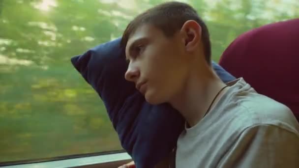 Il ragazzo riposa sul sedile del bus dal finestrino durante il viaggio. Bambino adolescente che viaggia in auto e si addormenta sul cuscino. Giovane stanco sul treno. Rifugiati dall'Ucraina. Da vicino. - Filmati, video