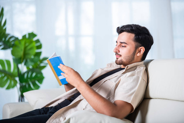 Indický asijské pěkný mladý muž čte knihu doma na pohovce - Fotografie, Obrázek