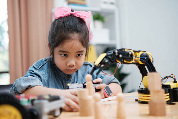 Дівчина початкової школи зосереджена на роботі з роботизованою рукою з пультом дистанційного керування, демонструючи STEM-освіту в дії. - Фото, зображення