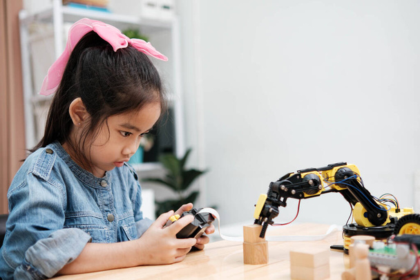 Een basisschool meisje richt zich op het bedienen van een robotarm met een afstandsbediening, demonstreren STEM onderwijs in actie. - Foto, afbeelding