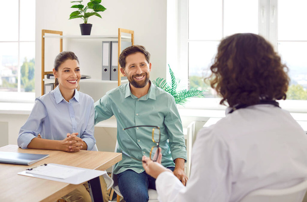 Cheerful family couple visiting doctor together. Happy married man and woman patients sitting at table, listening to doctor and smiling. Health care, planning for pregnancy, IVF treatment concept - Fotoğraf, Görsel