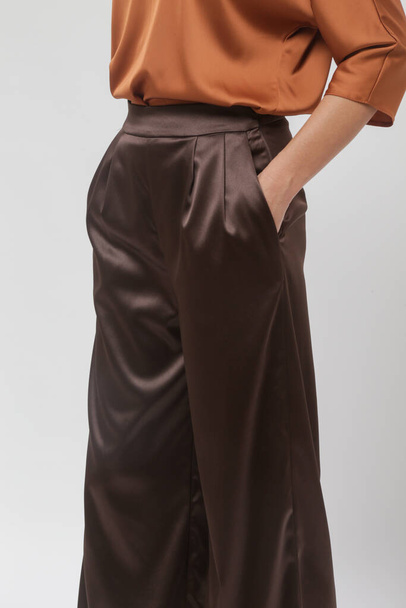 Sorozata stúdió fotók fiatal női modell visel egyszerű szép ruhát, selyem szatén barna blúz és széles lábú nadrág - Fotó, kép