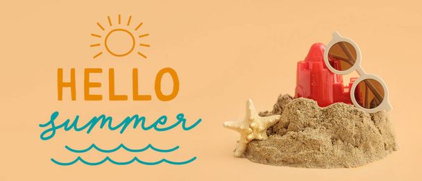 Castello di sabbia con giochi da spiaggia, stelle marine, occhiali da sole e testo HELLO SUMMER su sfondo beige - Foto, immagini