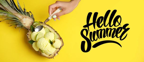 Main de femme mangeant une délicieuse crème glacée à l'ananas et texte HELLO, ÉTÉ sur fond jaune - Photo, image