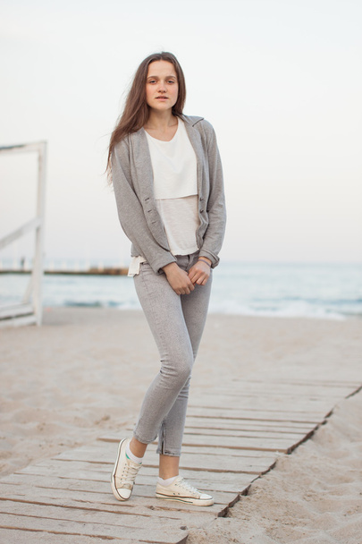 Fashionable portrait of a girl posing on the beach at sunset in a stylish comfortable clothing. Young woman outdoors - 写真・画像
