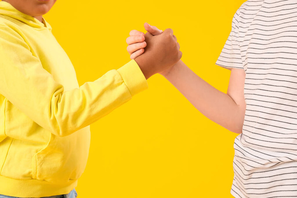 Μικρά αγόρια κρατιούνται χέρι-χέρι σε κίτρινο φόντο, κοντινό πλάνο. Γιορτή της ημέρας των παιδιών - Φωτογραφία, εικόνα