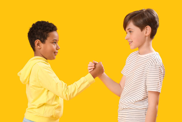 Μικρά αγόρια που κρατιούνται χέρι-χέρι σε κίτρινο φόντο. Γιορτή της ημέρας των παιδιών - Φωτογραφία, εικόνα