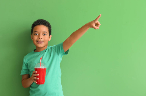 Un niño afroamericano con una taza de refresco apuntando a algo sobre un fondo verde. Celebración del Día de los Niños - Foto, imagen