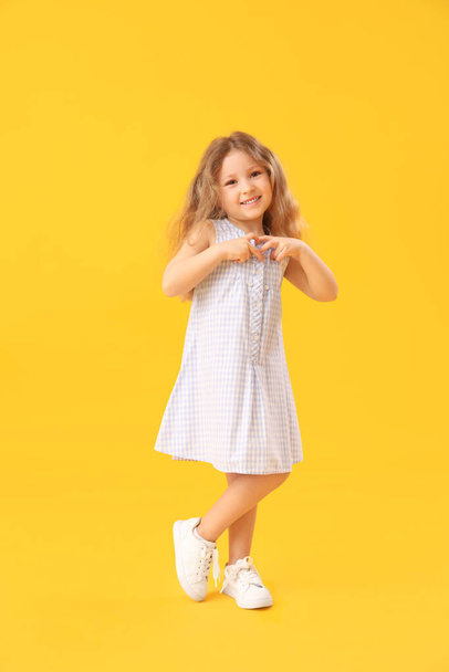 Küçük kız ellerini sarı arka planda tutarak kalp yapıyor. Çocuk Bayramı kutlaması - Fotoğraf, Görsel