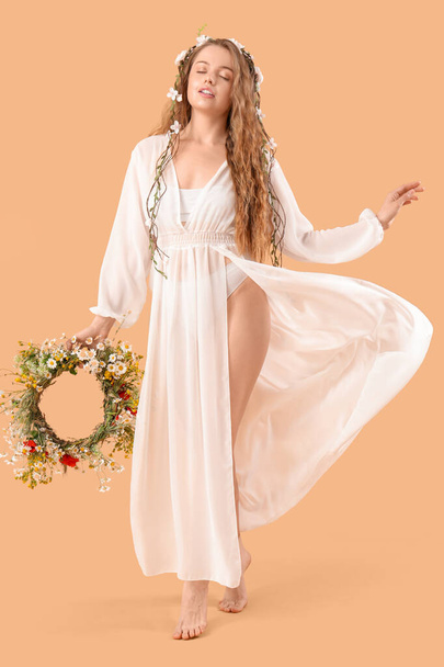 Beautiful young woman with flower wreath on beige background. Summer solstice - Photo, image