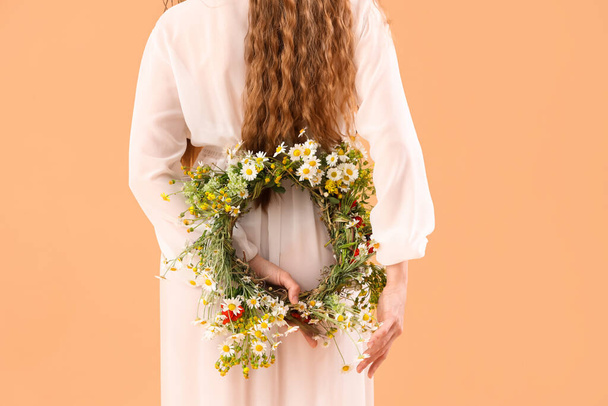 Beautiful young woman with flower wreath on beige background, back view. Summer solstice - Fotó, kép