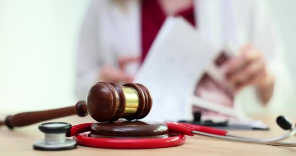 Gavel de juge en bois sur une table de médecin avec stéthoscope et médecin flou en arrière-plan. Examen médico-légal - Séquence, vidéo