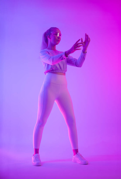Futurystyczna koncepcja z kobietą w okularach holograficznych, oświetlona żywymi neonowymi różowymi i niebieskimi światłami, przedstawiająca estetykę cyberpunku. - Zdjęcie, obraz