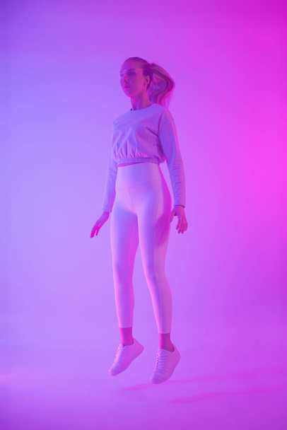 A fashionable young woman levitating in a vibrant neon-lit environment, exuding a sense of modern style and surrealism. - Photo, Image