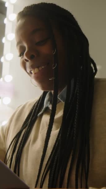 Вертикальний низький кут гумористичної афроамериканської жінки з плетеною зачіскою, що сидить перед дзеркалом з лампочками в роздягальні і сміється над анекдотами перед концертом стенда - Кадри, відео