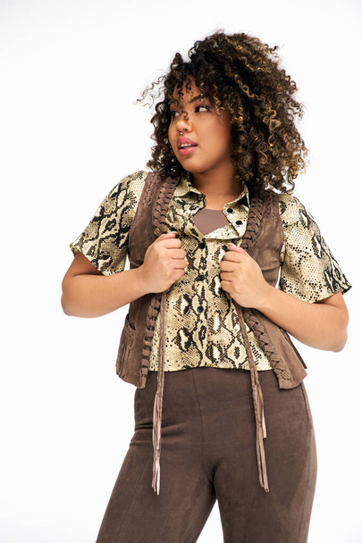 stylish young african american woman with animalistic print on outfit looking away on white backdrop - Foto, Imagen