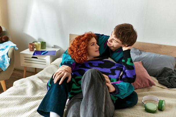 κομψό χαρούμενο ζευγάρι σε casual άνετο ντύσιμο ξοδεύει χρόνο στο σπίτι και αγκαλιάζει στοργικά στο κρεβάτι - Φωτογραφία, εικόνα