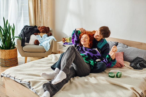 svůdný veselý pár ve stylovém pulzujícím oblečení ležící spolu v posteli a láskyplně objímající - Fotografie, Obrázek