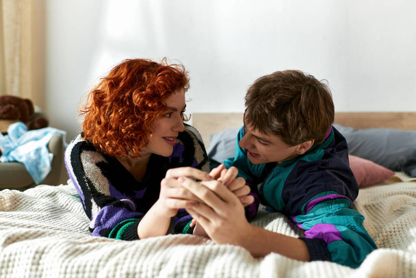 cheerful trendy couple in casual vivid outfits lying in bed together while spending time at home - Photo, Image