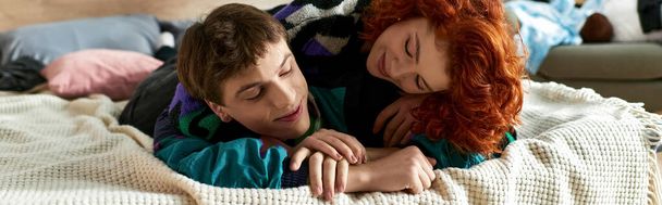 knappe man ontspannen in bed naast zijn rood haar verleidelijke vriendin terwijl thuis, banner - Foto, afbeelding