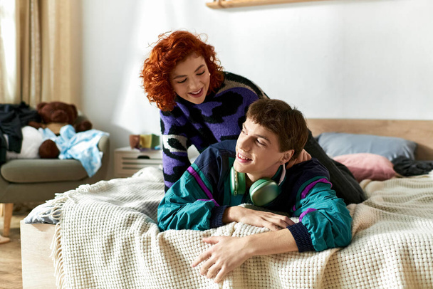 красивый молодой человек с наушниками лежал рядом со своей любящей рыжеволосой девушкой на кровати - Фото, изображение