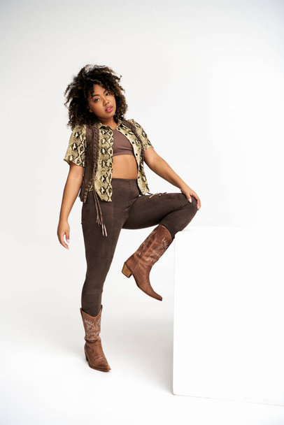 elegancka Afroamerykanka z animalistycznym nadrukiem na ubraniu obok sześcianu patrząca w kamerę - Zdjęcie, obraz