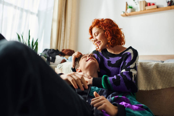 joyous appealing woman with red hair hugging lovingly her handsome cheerful boyfriend at home - Photo, Image