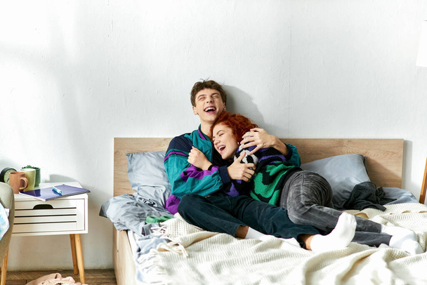 радостная привлекательная пара в ярких модных нарядах обнимающая и смеющаяся в постели дома - Фото, изображение
