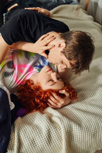 gut aussehendes schickes Paar in Homewear, das sich auf einen liebevollen Kuss vorbereitet, während es zusammen im Bett liegt - Foto, Bild