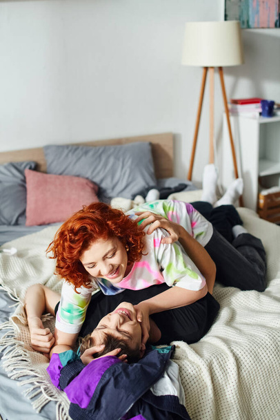 attraktives, fröhliches Paar in Homewear, das sich darauf vorbereitet, sich liebevoll zu küssen, während es zusammen im Bett liegt - Foto, Bild