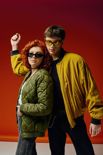 attraente coppia alla moda in abiti eleganti con occhiali da sole in posa su sfondo rosso insieme - Foto, immagini