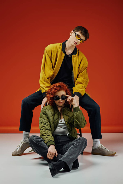 giovane uomo alla moda in occhiali da sole alla moda in posa accanto alla sua bella fidanzata dai capelli rossi - Foto, immagini