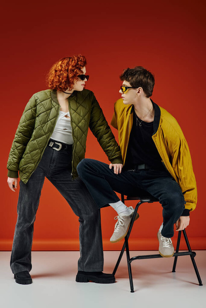 young man in fashionable attire with sunglasses sitting on chair next to his red haired girlfriend - Foto, afbeelding