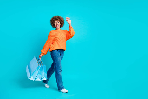 Full size profile photo of positive girl hold mall bags walk arm wave hi empty space isolated on teal color background. - Foto, Imagem