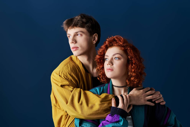 beautiful woman and her boyfriend in vibrant clothes hugging and looking away on blue backdrop - Photo, Image