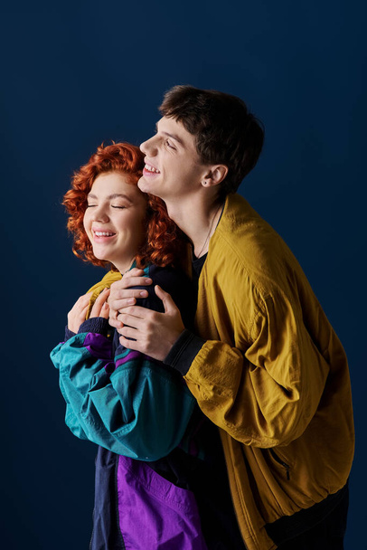 χαρούμενο ελκυστικό ζευγάρι με πολύχρωμα κομψά ρούχα αγκαλιάζει στοργικά και χαμογελώντας ευτυχισμένα - Φωτογραφία, εικόνα