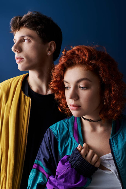 заманчивый парень и рыжеволосая девушка позируют вместе на темно-синем фоне и смотрят в сторону - Фото, изображение