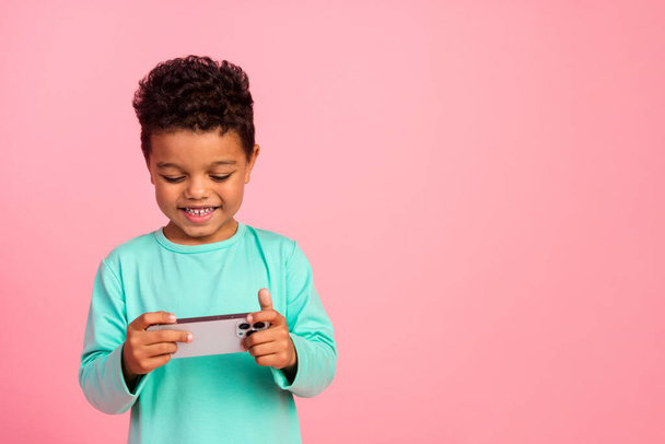 Portrait photo de charmant petit garçon jouer jeu mobile avoir du plaisir porter tenue aquamarine tendance isolé sur fond de couleur rose. - Photo, image