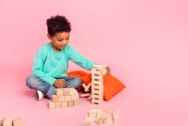 Full body foto van schattig jongetje spelen jenga houten blokken spel dragen trendy aquamarijn kleding geïsoleerd op roze kleur achtergrond. - Foto, afbeelding