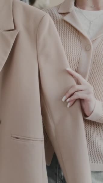 Verticale bijgesneden slowmo schot van onherkenbare vrouwelijke mode stylist demonstreren elegante beige pak jas op hanger op camera tijdens het opnemen van video blog in stijlvolle kledingwinkel - Video