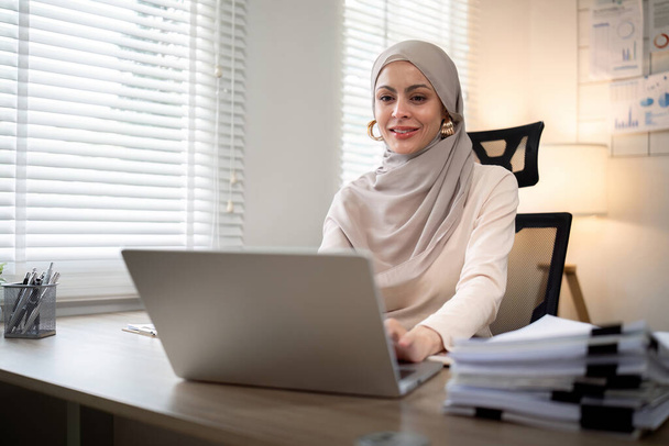 Aasian muslimien liikenainen hijabhuivissa työskentelee paperilla nykyaikaisessa toimistossa. monimuotoisuus ja toimistokäsite. - Valokuva, kuva