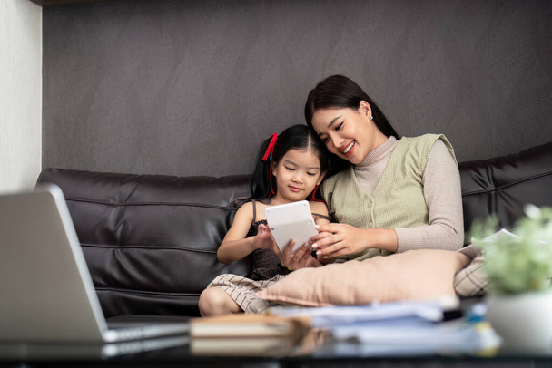 Geschäftsfrau oder Mutter, die mit ihrer kleinen Tochter am Laptop arbeitet. Freiberuflich, Arbeit von zu Hause aus. - Foto, Bild